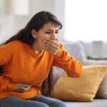 Sick young Indian woman sitting in the couch suffering from food poisoning and nausea. home remedies for nausea concept