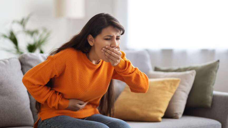 Sick young Indian woman sitting in the couch suffering from food poisoning and nausea. home remedies for nausea concept