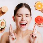 Portrait of young girl with closed eyes on white background with oranges and avocado for healthy skin