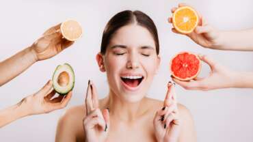 Portrait of young girl with closed eyes on white background with oranges and avocado for healthy skin