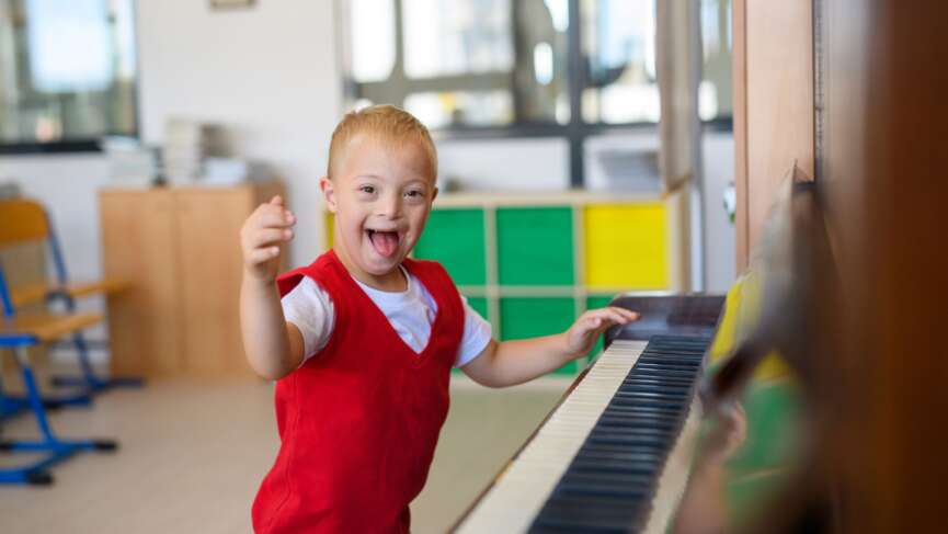 Cute boy playing piano with down syndrome in a red sweater