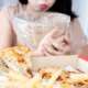 a girl with a disease and symptoms of Bulimia nervosa with a pizza on the table and her being about to puke in background, often called bulimia, is a type of eating disorder