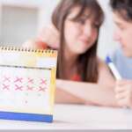 calendar with marked missed period and cancel mark and a couple in a background discussing sexual health and pregnancy after period