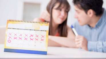 calendar with marked missed period and cancel mark and a couple in a background discussing sexual health and pregnancy after period