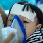 A young mother helping her son to inhale with a nebulizer at home, representing pneumonia treatment at home