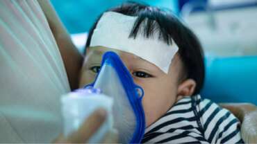 A young mother helping her son to inhale with a nebulizer at home, representing pneumonia treatment at home