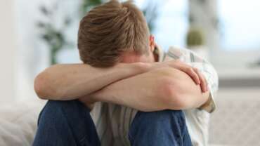 A hopeless man sitting alone, hugging his knees on the floor representing signs of depression
