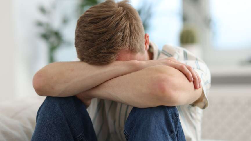 A hopeless man sitting alone, hugging his knees on the floor representing signs of depression