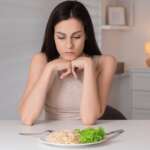 An eating disorder sad woman with fork and spaghetti over a plate, representing facts about bulimia