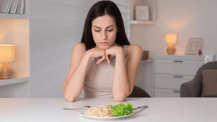 An eating disorder sad woman with fork and spaghetti over a plate, representing facts about bulimia
