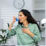 woman using asthma inhaler sitting in hospital experiencing breathing symptoms of asthma