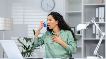 woman using asthma inhaler sitting in hospital experiencing breathing symptoms of asthma