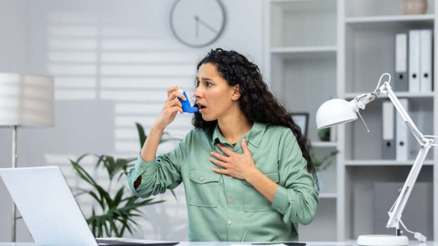 woman using asthma inhaler sitting in hospital experiencing breathing symptoms of asthma