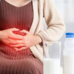 A young woman with a bottle of milk and half glass of milk on the table in front is having painful stomachache, representing effective ways to beat bloating