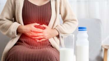 A young woman with a bottle of milk and half glass of milk on the table in front is having painful stomachache, representing effective ways to beat bloating