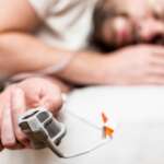 Close-up of ill man sleeping on bed with home sleep apnea test kit at fingertip