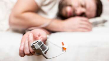Close-up of ill man sleeping on bed with home sleep apnea test kit at fingertip