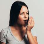 a girl covering a wide-open mouth with hand, representing home remedies for bad breathe