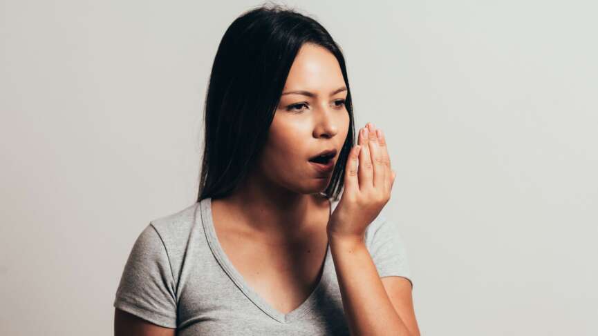 a girl covering a wide-open mouth with hand, representing home remedies for bad breathe