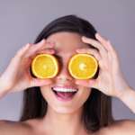 Close-up of a smiling woman placing oranges on her eyes representing best eye vitamins