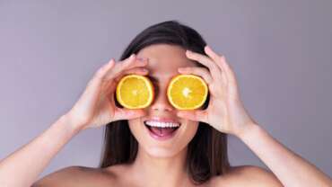 Close-up of a smiling woman placing oranges on her eyes representing best eye vitamins