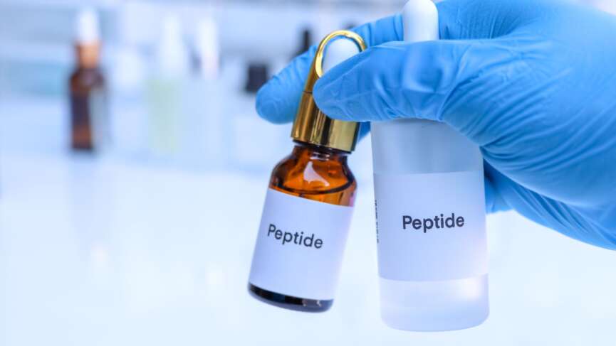 a man holding a two bottle of peptides with a blue gloves for hair loss treatment