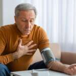 A mature man checking his blood pressure with a digital blood pressure monitor at home, portraying causes of high blood pressure