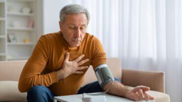 A mature man checking his blood pressure with a digital blood pressure monitor at home, portraying causes of high blood pressure