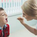 A young pediatrician examining little boy's throat to diagnose his illness, either from sore throat or strep throat