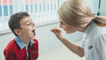 A young pediatrician examining little boy's throat to diagnose his illness, either from sore throat or strep throat