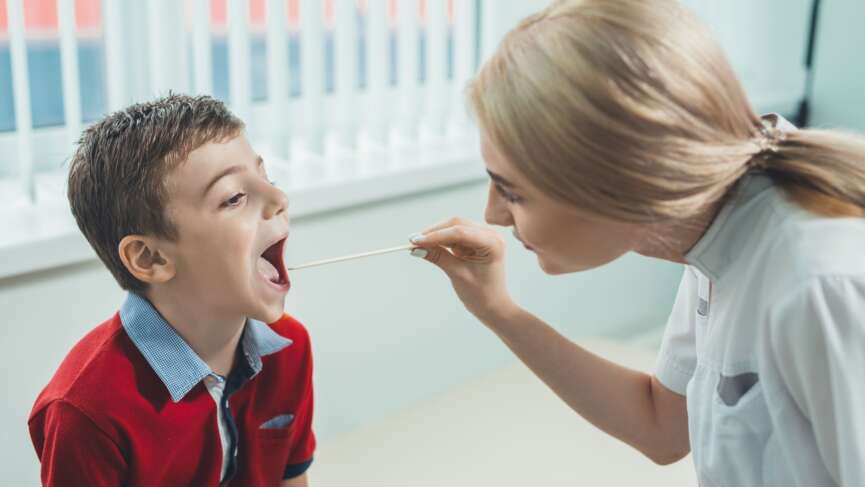 A young pediatrician examining little boy's throat to diagnose his illness, either from sore throat or strep throat