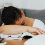 A tired young woman feeling excessive sleepiness, head down on table and with a couch in the background