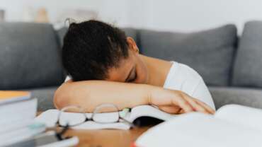 A tired young woman feeling excessive sleepiness, head down on table and with a couch in the background