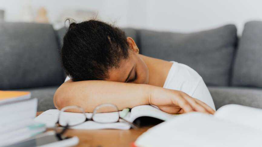 A tired young woman feeling excessive sleepiness, head down on table and with a couch in the background