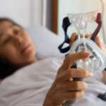 a sick woman holding oxygen therapy mask, lying in hospital bed