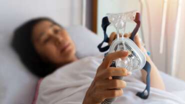 a sick woman holding oxygen therapy mask, lying in hospital bed