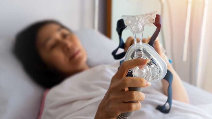 a sick woman holding oxygen therapy mask, lying in hospital bed