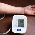 A man's arm with a device for taking blood pressure reading, machine showing high blood pressure of patient