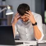 An eye-hurting, tired, overworking businessman with laptop on table and feeling of stress on his body