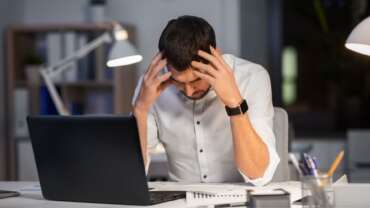 An eye-hurting, tired, overworking businessman with laptop on table and feeling of stress on his body