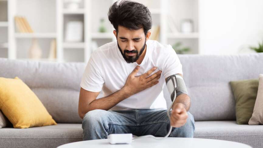 a young man sitting on couch and checking his blood pressure and cholesterol