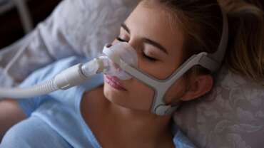 A woman wearing CPAP mask for sleep apnea treatment, related to types of sleep apnea