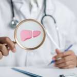 A doctor holding magnifier focused on liver organ icon for the diagnosis of liver biopsy
