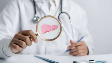 A doctor holding magnifier focused on liver organ icon for the diagnosis of liver biopsy