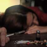 A woman holding syringe by pills and bottle on table due to opioid overdose