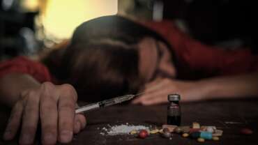 A woman holding syringe by pills and bottle on table due to opioid overdose