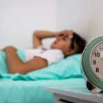 A sleepy young woman turns off signal of alarm clock due to sleep apnea