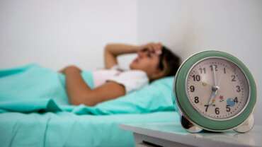 A sleepy young woman turns off signal of alarm clock due to sleep apnea