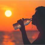 Person's silhouette drinking water at sunset during a heat wave. Causes of excessive thirst concept