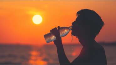 Person's silhouette drinking water at sunset during a heat wave. Causes of excessive thirst concept